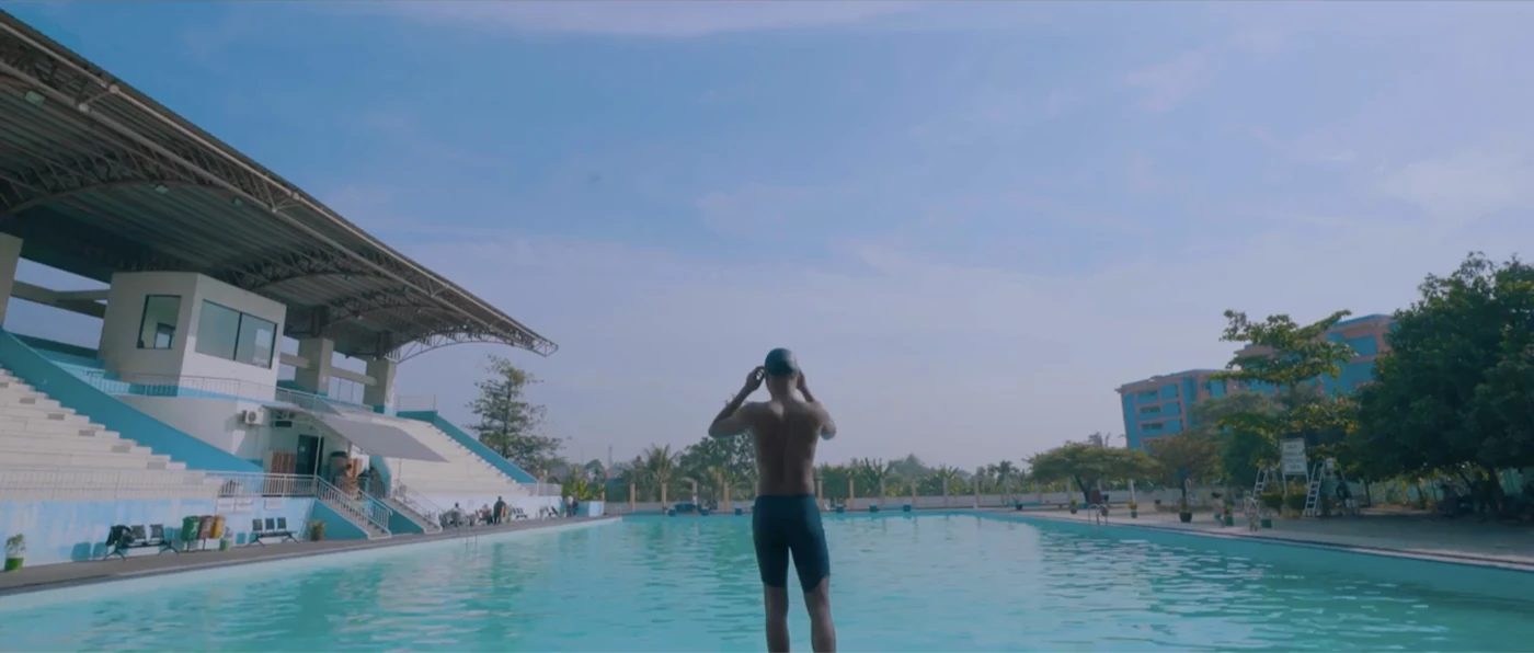 Still from a campaign film: a swimmer at an outdoor pool
